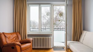 Uma sala de estar com um sofá de couro marrom, um sofá branco e uma janela com cortinas.