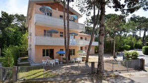 Un hotel de varios pisos con balcones, mobiliario exterior y un jardín cercado.