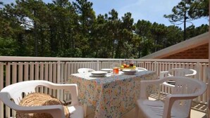 Un patio con una mesa preparada para dos personas, rodeado de sillas de plástico blanco, con vistas a pinos al fondo.