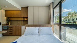 Ein modernes Hotelzimmer mit Bett, einer kleinen Küchenzeile und einem großen Fenster mit Blick nach außen.