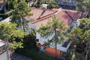 A multi-story building with a red-tiled roof, surrounded by trees. - Holiday flat with air conditioning and terrace (Lignano)