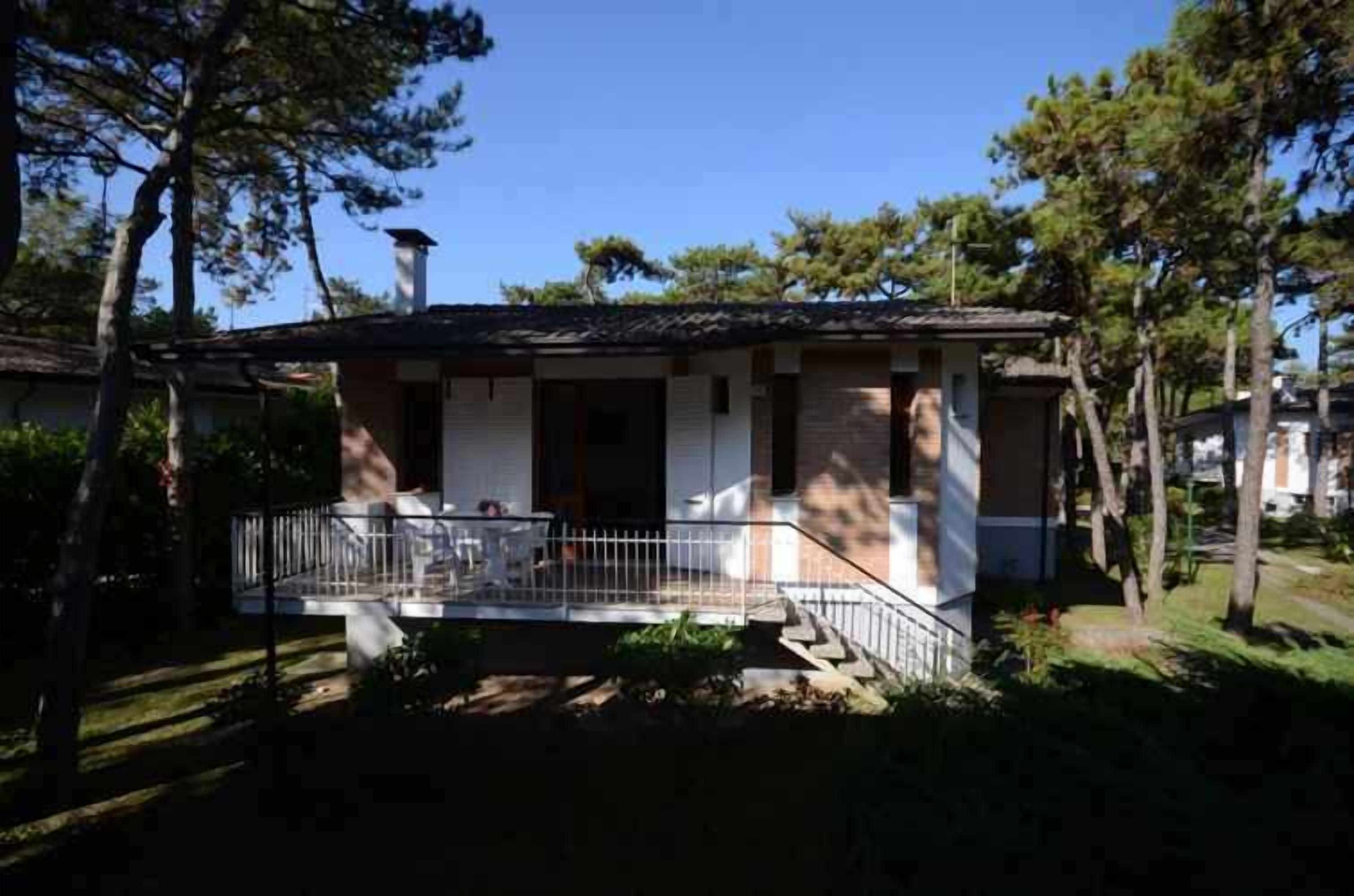 A two-story house with a balcony, surrounded by trees.