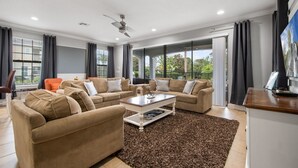Un salon spacieux avec un canapé d’angle beige, une table basse et une grande fenêtre donnant sur un paysage verdoyant.
