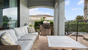 Une terrasse extérieure avec un canapé gris, une table en bois et un barbecue en pierre.
