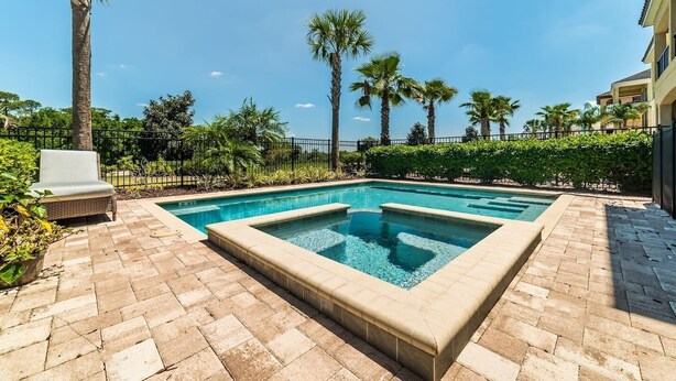Une piscine rectangulaire bordée de carreaux, entourée d’une terrasse en briques. Un fauteuil de jardin en osier se trouve à gauche de la piscine.