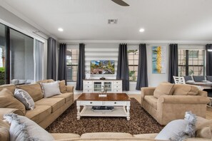 A modern living room with a beige sofa set, a wooden coffee table, and a flat-screen TV. - 5 Bedroom Reunion Home | Pool Spa and Themed Rooms (Kissimmee)