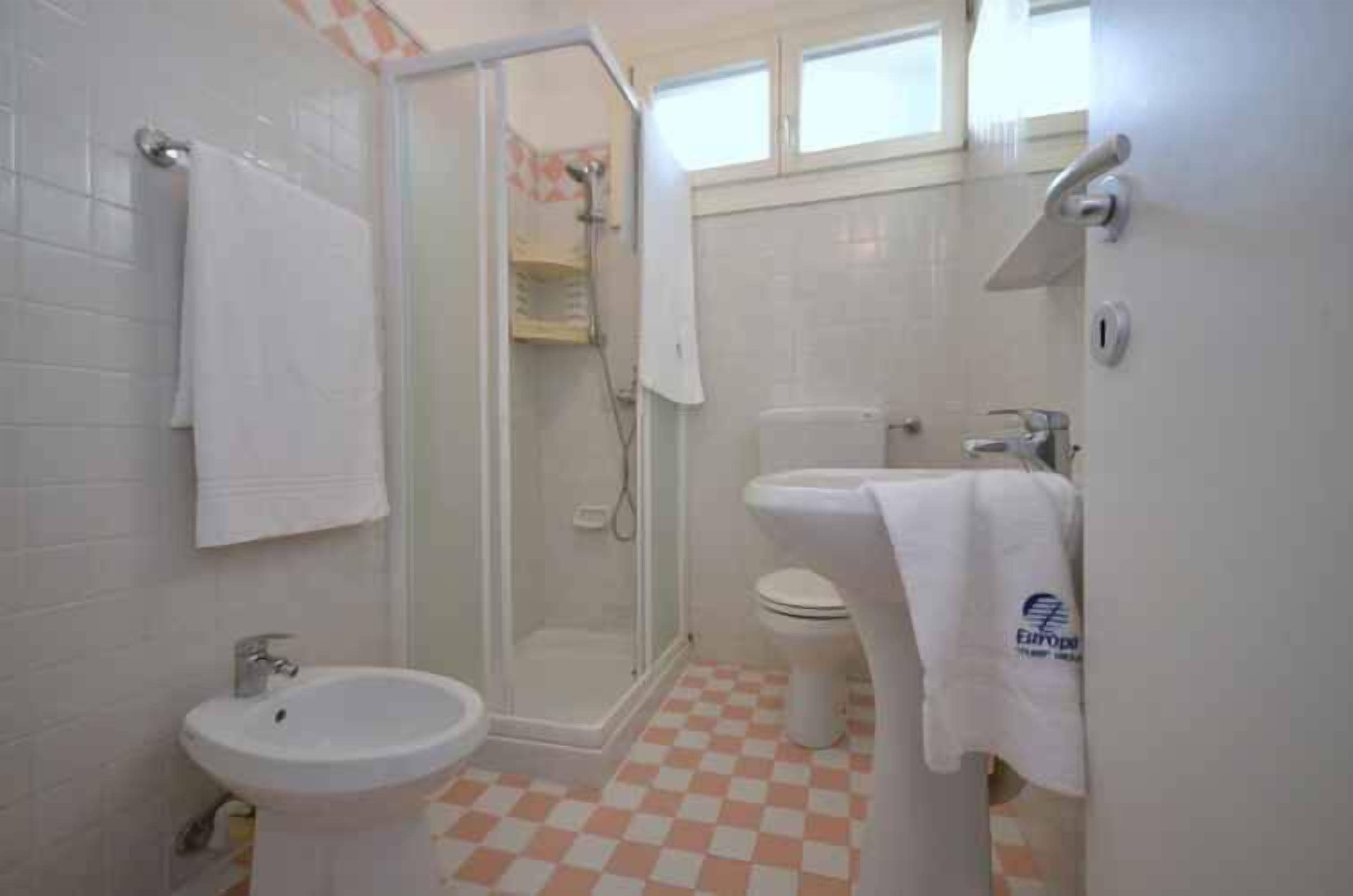 A bathroom with a shower, toilet, sink, and a checkered floor.