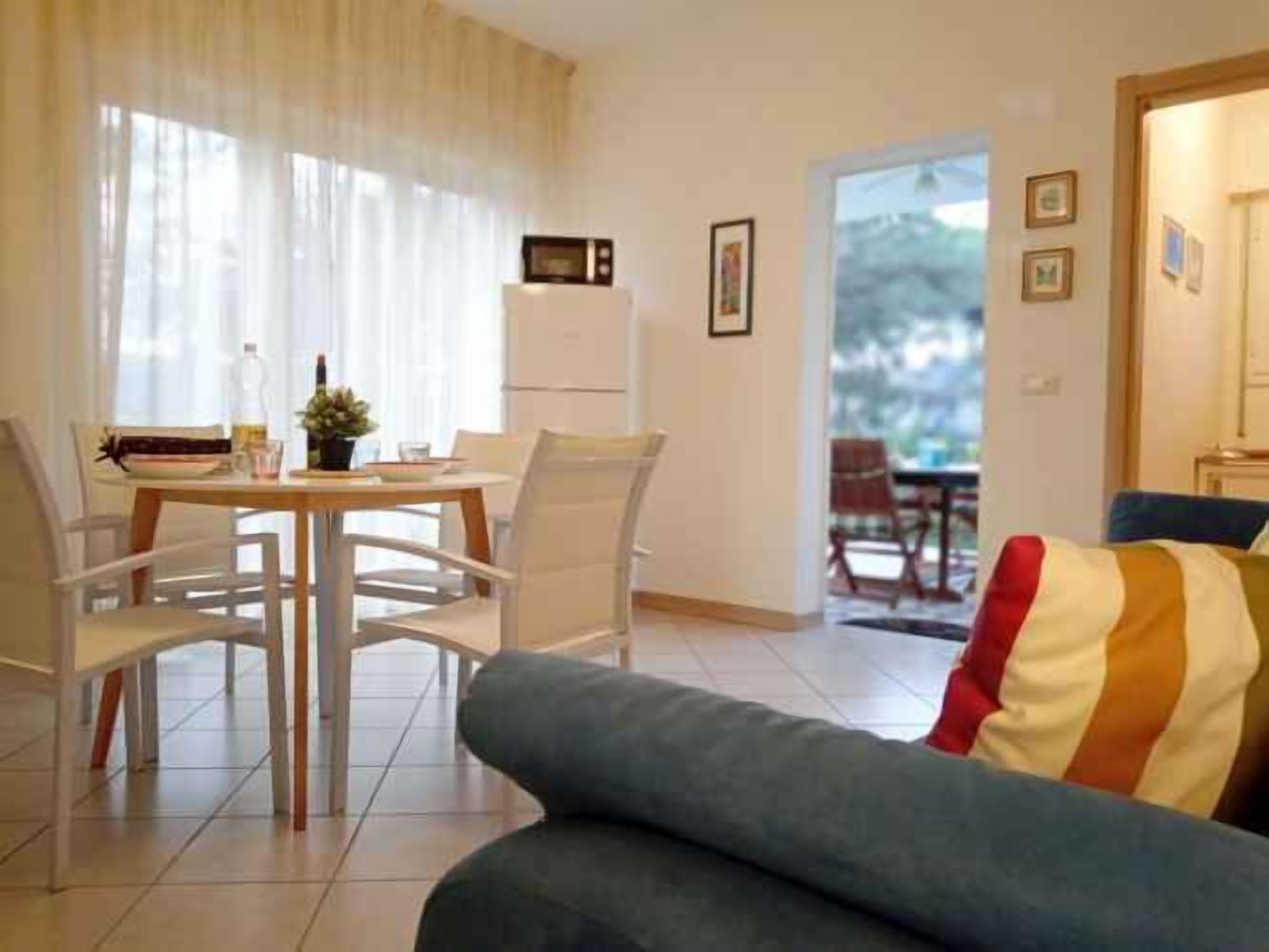 A modern living room with a sofa, a dining table with chairs, a microwave, and a refrigerator.