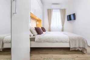 A bedroom with a bed, curtains, a TV, and a wooden headboard. - Holiday Apartment Holiday Apartment Mateja with Air Conditioning and Terrace (Njivice)