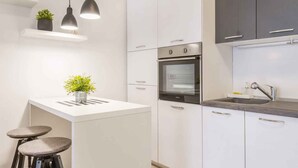 Eine moderne Küche mit weißen Schränken, einem eingebauten Backofen, einer Spüle, Pendelleuchten und zwei Barhocker.
