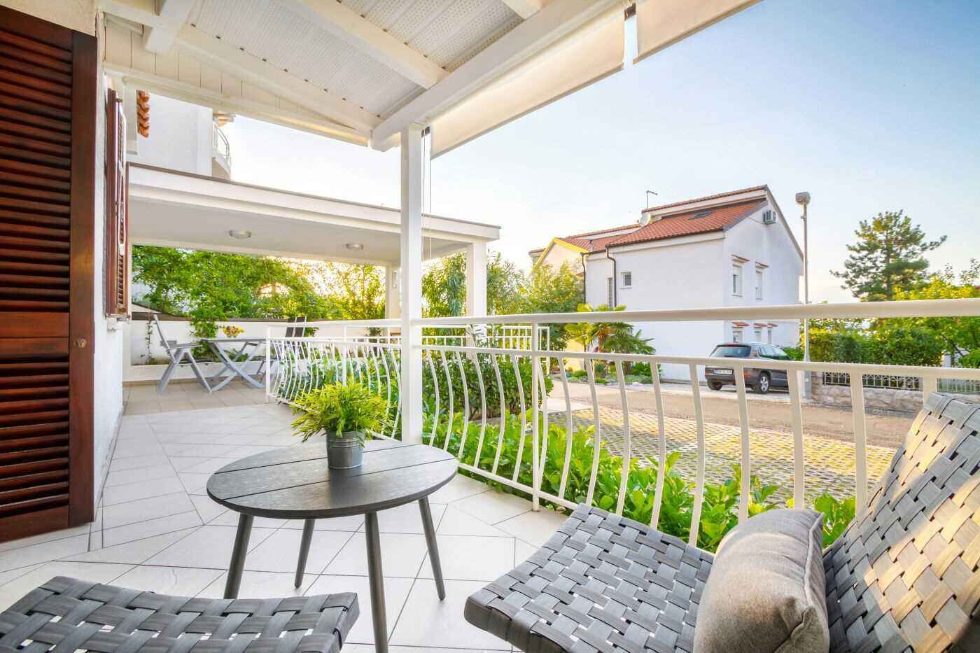 A covered outdoor area with a table and chairs, a potted plant, and a view of a street and buildings.