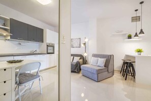 A modern kitchen with grey cabinets, a dining area with a grey chair, a grey sofa, and a small bar area with stools. - Holiday Apartment Holiday Apartment Mateja with Air Conditioning and Terrace (Njivice)