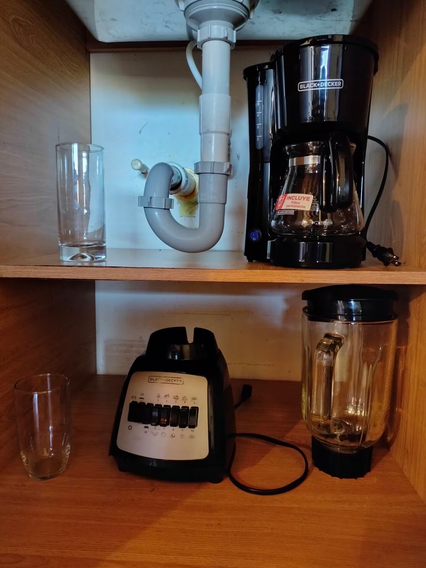 A kitchen with a coffee maker, a blender, and a glass on the counter.