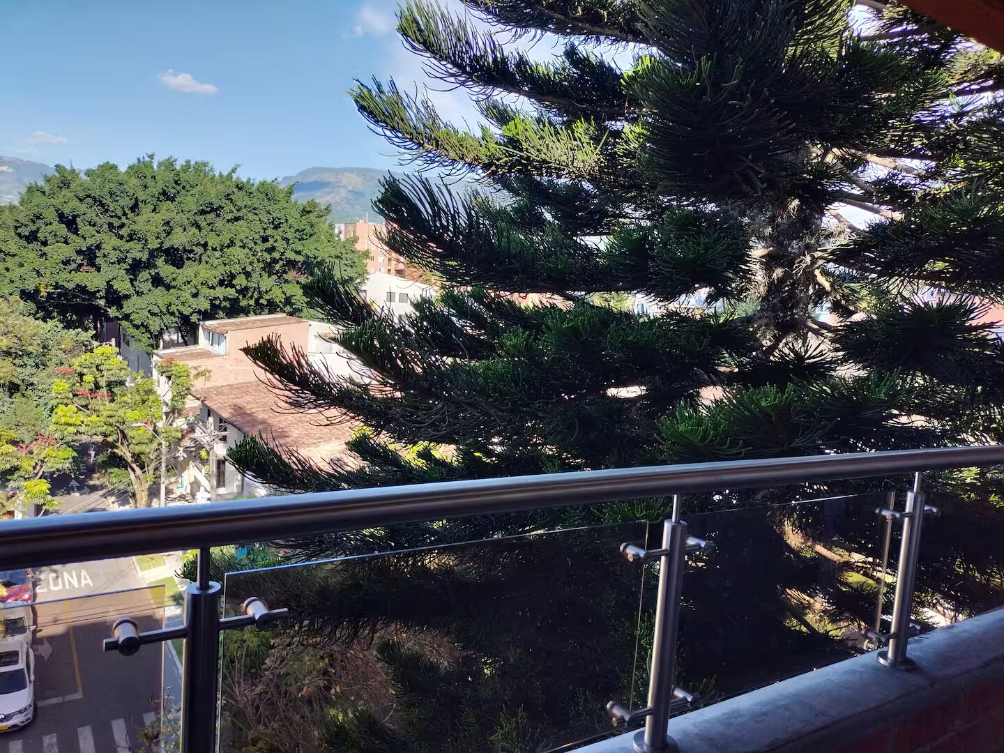 Un balcon doté d’une rambarde en métal, donnant sur une rue bordée de voitures garées et d’immeubles.