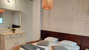 En pænt redt seng med puder og dyne, en kommode med skuffer, et spejl og en hængende lampe.