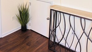Habitació amb televisió plana penjada, una porta blanca, una planta en test i una taula de consola amb estructura de metall.