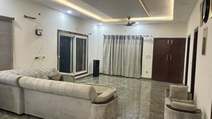 A modern living room with a sectional sofa, a small ottoman, a ceiling fan, and a sliding glass door. - Luxury 2BHK Villa with Private Pool – Sector 135, Noida (Noida)