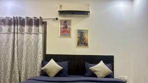 A bedroom with a bed, two pillows, an air conditioner, and two framed pictures on the wall. - Luxury 2BHK Villa with Private Pool – Sector 135, Noida (Noida)