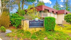 A Riverstone condominium with a stone sign, surrounded by lush greenery and trees. - Cozy Work-ready 1BR Condo Near Downtown (Bellevue)