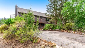 A two-story house with a balcony, surrounded by dense greenery and a paved driveway. - 3BR with Epic Mountain Views and Huge Deck! (Estes Park)