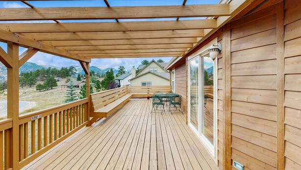A wooden deck with a pergola, a table with chairs, and a view of houses and mountains. - Conveniently located home w/ full kitchen, w/d, deck & mountain views (Estes Park)