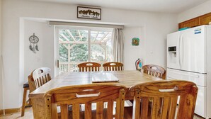 A dining area with a wooden table and chairs, a white refrigerator, and a window with a view of trees. - Conveniently located home w/ full kitchen, w/d, deck & mountain views (Estes Park)