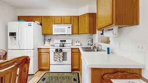 A compact kitchen with wooden cabinets, a white refrigerator, a microwave, a stove, and a sink. - Conveniently located home w/ full kitchen, w/d, deck & mountain views (Estes Park)