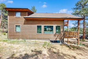 A wooden cabin with a deck, large windows, and a small upper balcony. - Modern cabin with mountain views, private yard & furnished deck - great location (Estes Park)