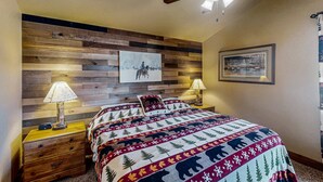 Una camera da letto con una testiera in legno, un letto con copripiumino decorato, due comodini con lampade e una ventola a soffitto.
