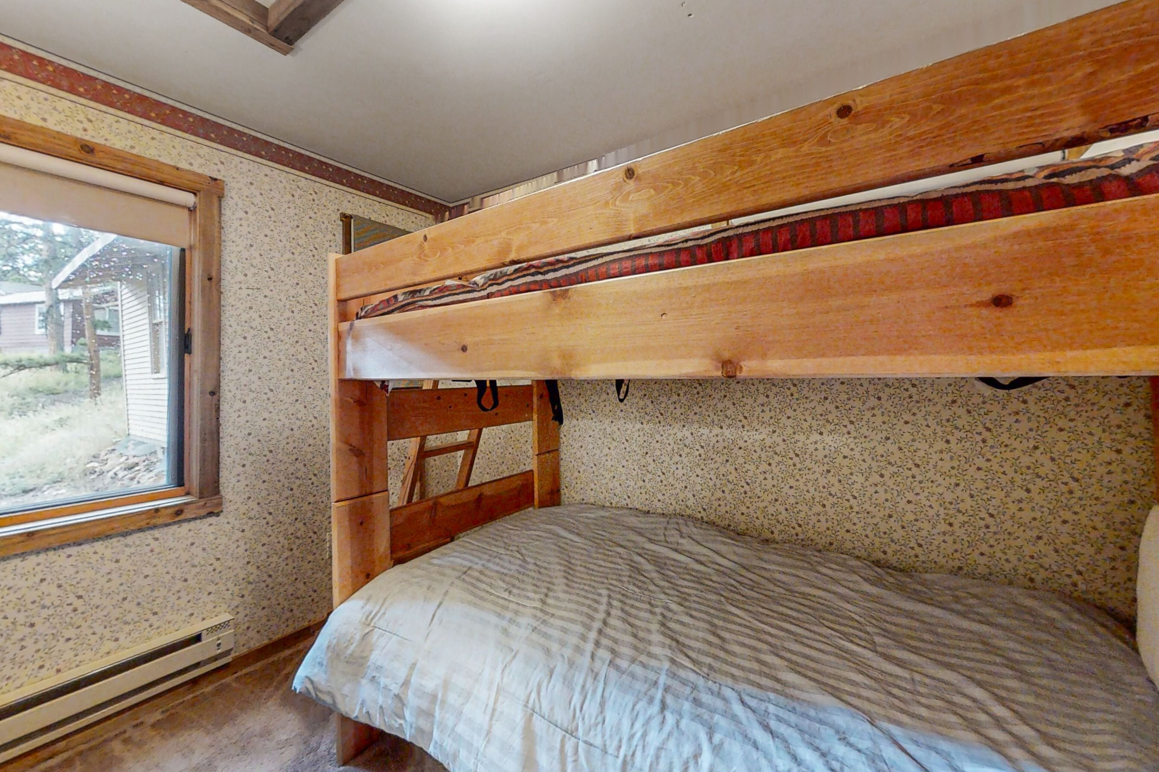 Une chambre avec un lit superposé, une fenêtre, une tête de lit en bois et une couvre-lit matelassé.