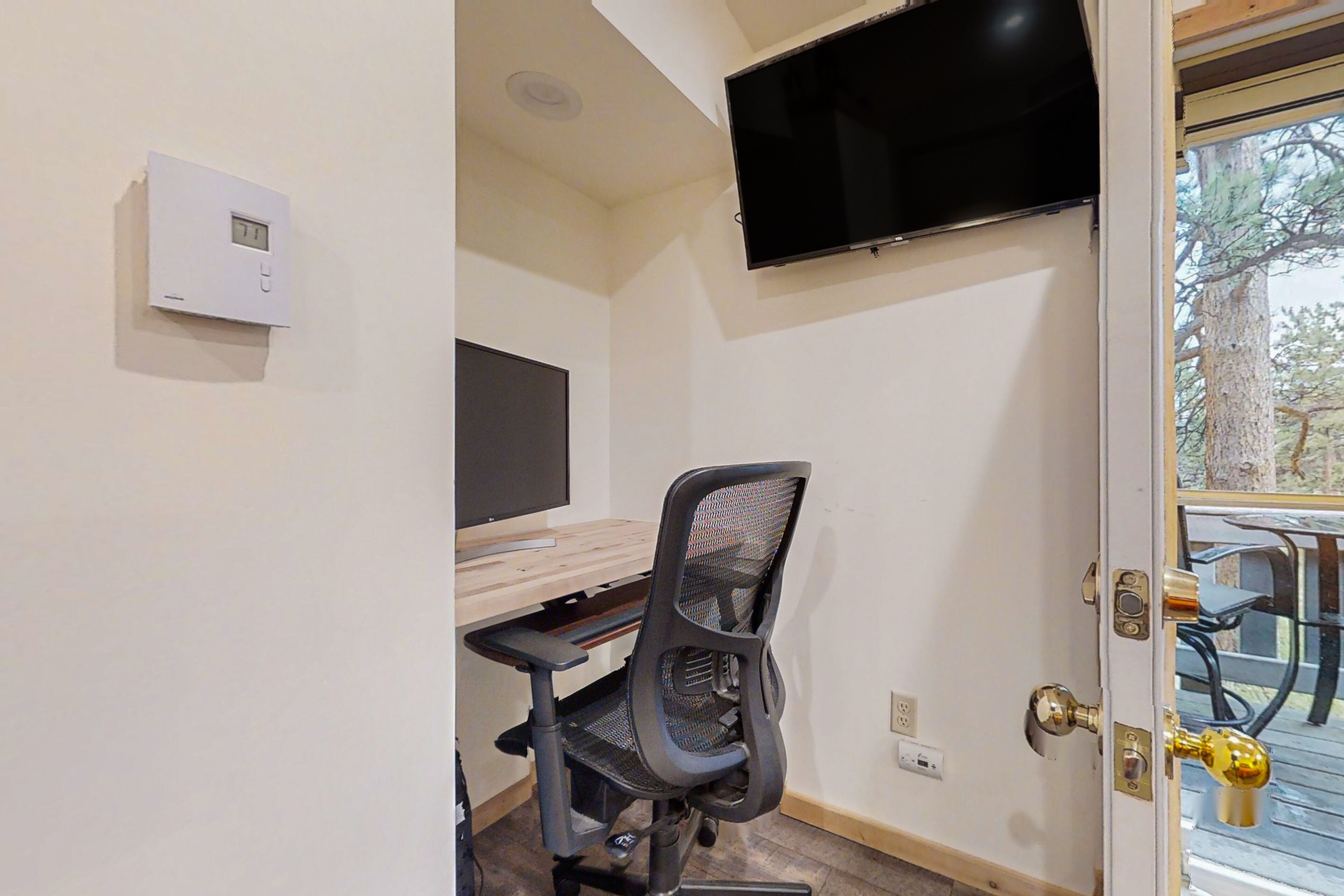 Habitación con escritorio, silla, televisor, termostato y puerta que da a un área exterior.
