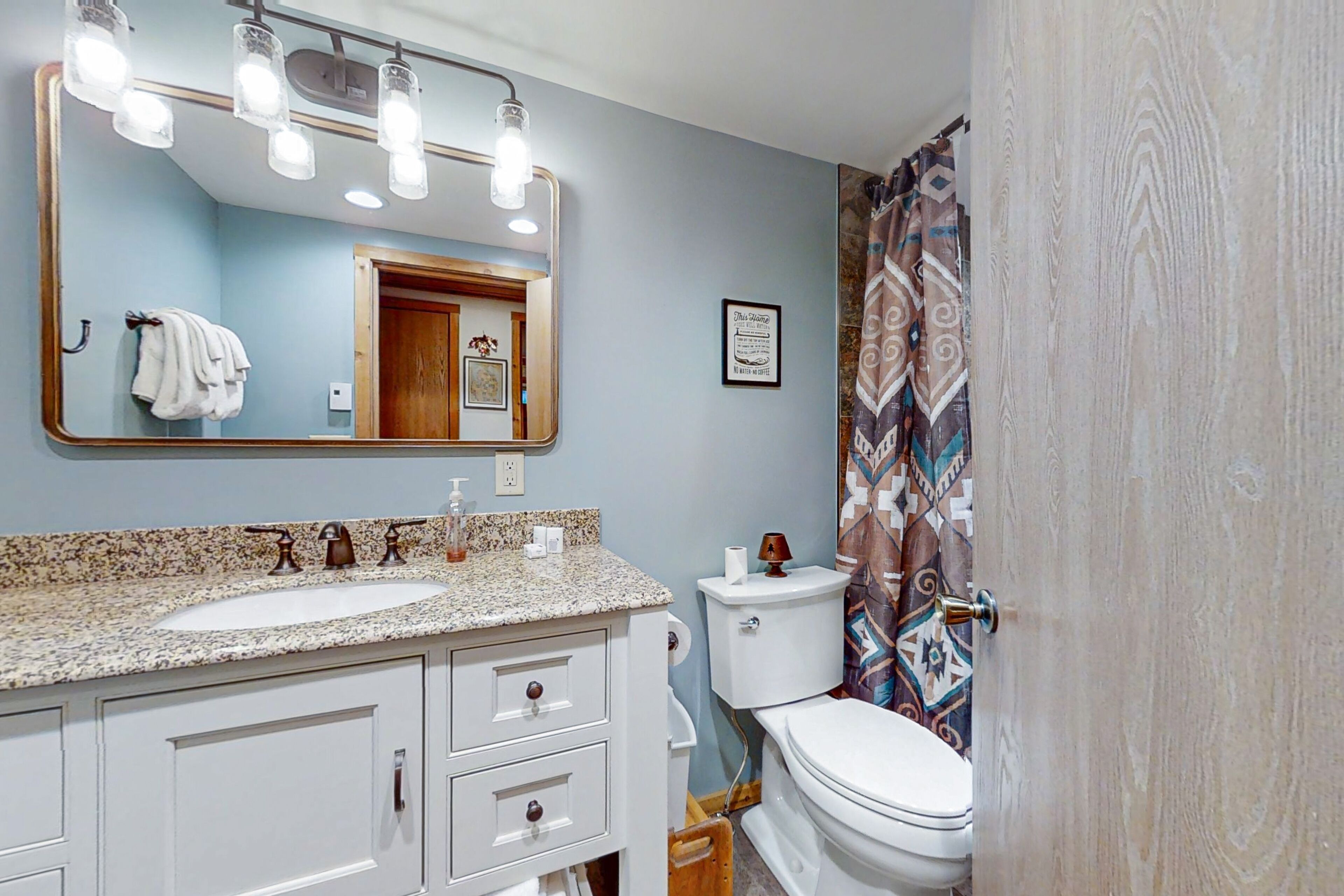 A bathroom with a granite countertop sink, a large mirror, a toilet, and a shower curtain.