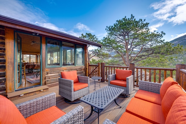 Une terrasse en bois, agrémentée de meubles en osier et de coussins orange, qui offre une vue sur un paysage montagneux.