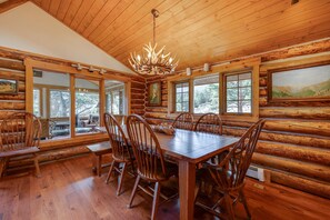 L’intérieur d’une cabane en rondins, avec une grande table à manger en bois, plusieurs chaises et un lustre.