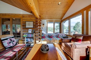 L’intérieur d’un chalet accueillant, avec un plafond en bois, de grandes fenêtres, un canapé, un fauteuil et une bibliothèque.
