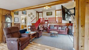 Ein gemütliches Wohnzimmer mit einem braunen Sofa, einem Fernseher mit rotem Rahmen und einer Treppe, die eine weitere Ebene hinaufführt.