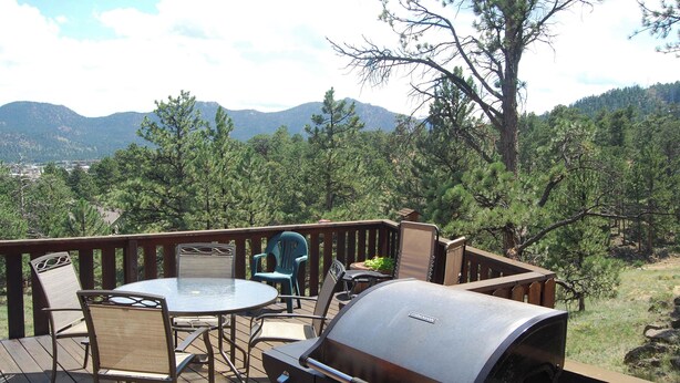Eine Terrasse mit Grill, Stühlen und Tisch mit Blick auf ein bewaldetes Gebiet und Berge im Hintergrund.