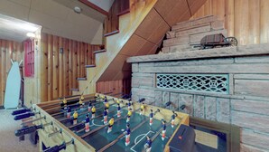 Ein Zimmer mit Kicker, Holzwänden, einem Steinofen und einer Treppe.