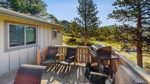 A deck with outdoor furniture, a grill, and a view of a forested area. - Enjoy nature from this charming cabin with deck, fireplace, & washer/dryer (Estes Park)