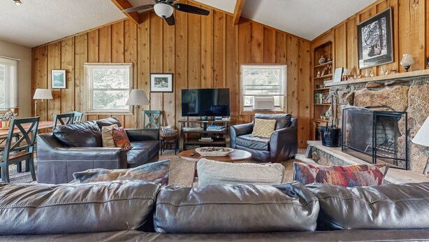 A cozy living room with wooden walls, a fireplace, leather sofas, and a television. - Enjoy nature from this charming cabin with deck, fireplace, & washer/dryer (Estes Park)