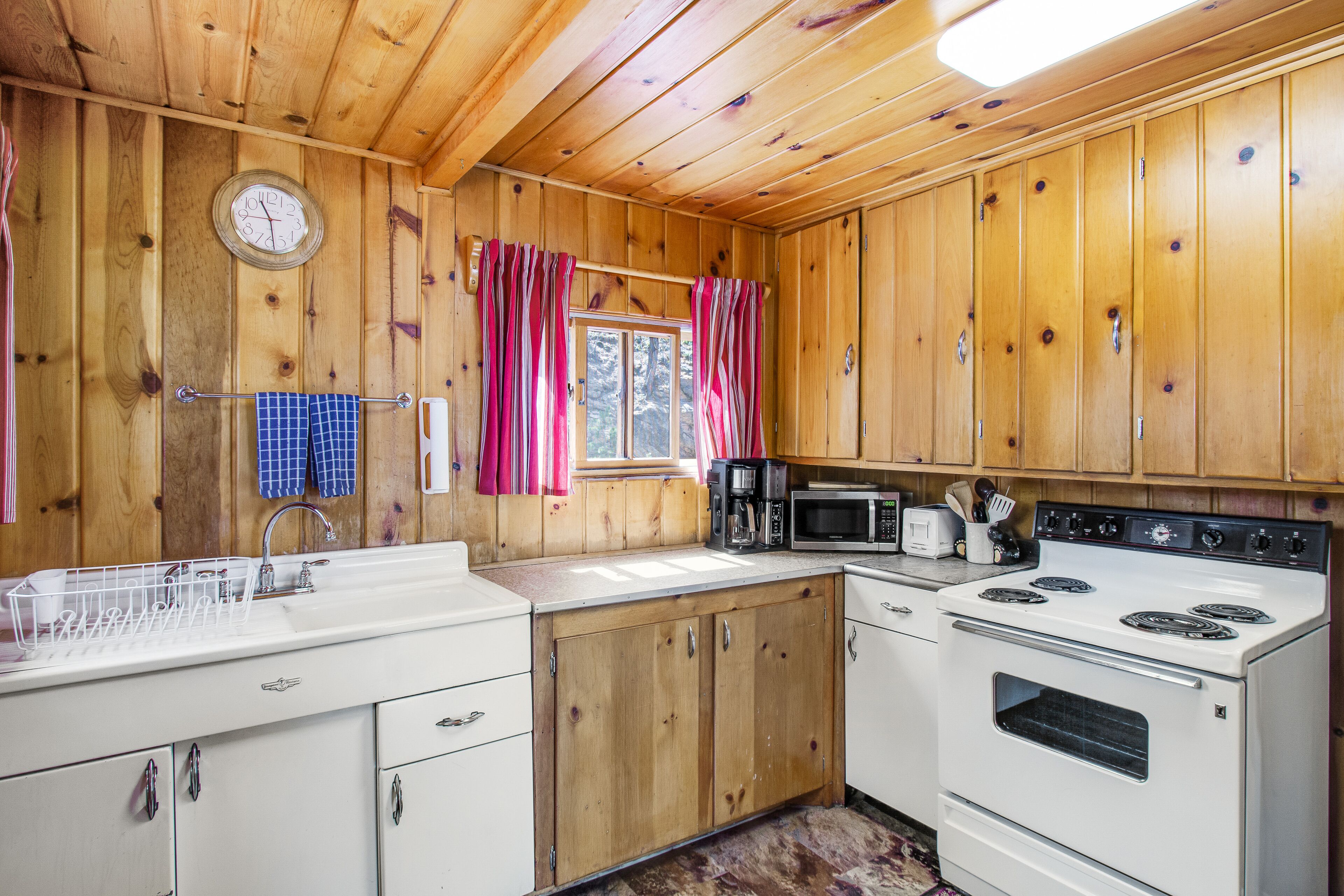 Cocina de cabaña de madera con estufa blanca, microondas y fregadero.