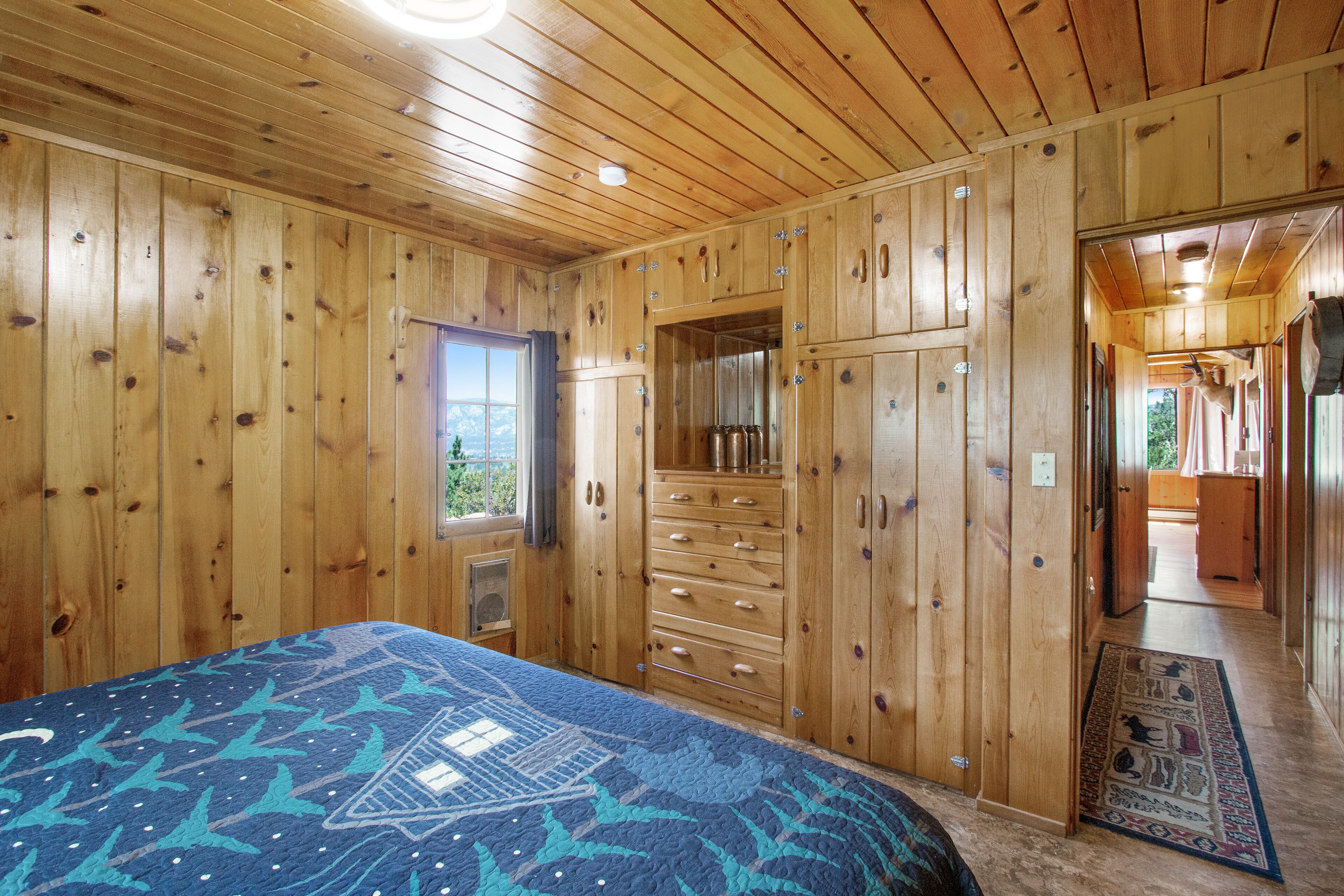 A wooden cabin bedroom with a bed, dresser, and a window with a view.