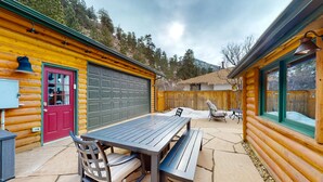 En træhytte med en terrasse, der har et bord og bænke, en rød dør og en garage.