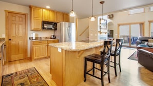A spacious kitchen with wooden cabinets, stainless steel appliances, and a granite countertop island with bar stools. - 3BR Three-story home with epic mountain views & fireplace (Estes Park)