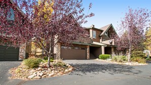 A two-story house with a garage, a stone foundation, and a well-maintained front yard with rocks and shrubs. - 3BR Three-story home with epic mountain views & fireplace (Estes Park)