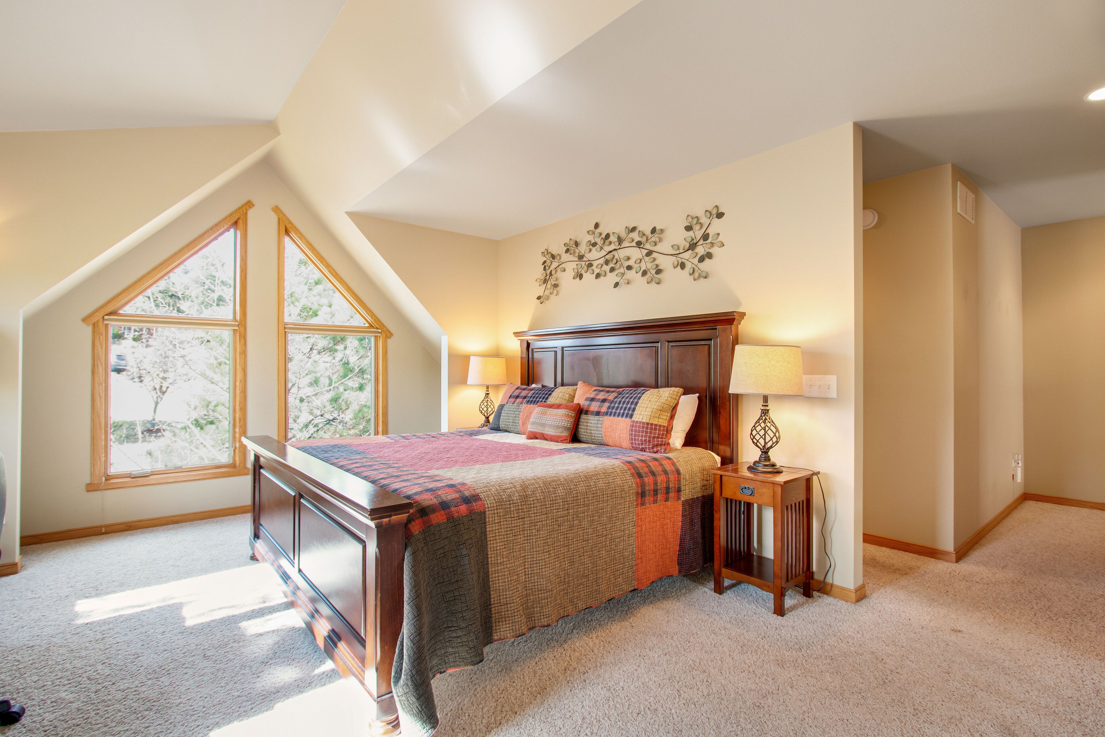A bedroom with a large window, a bed with a quilt, a nightstand, and a wall decoration.