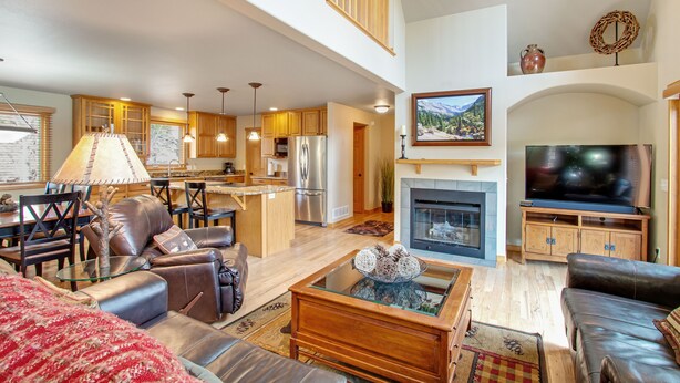 A spacious living area with a fireplace, a television, and a kitchen in the background. - 3BR Three-story home with epic mountain views & fireplace (Estes Park)