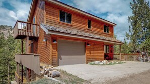 Eine zweistöckige Holzhütte mit Balkon, Garage und Natursteinfundament.