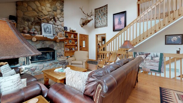 Ein gemütliches Wohnzimmer mit Kamin aus Stein, einer Ledersofa, einer Holztreppe und verschiedenen Wanddekorationen.