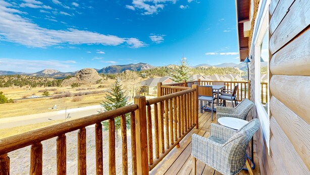 A wooden deck with wicker furniture and a clear view of mountains and a road. - Memorable mountain condo with 2 fireplaces, lovely views, W/D, & pool access (Estes Park)